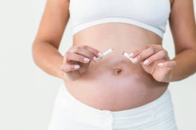 Close-up of pregnant woman destroying cigarette against white background
