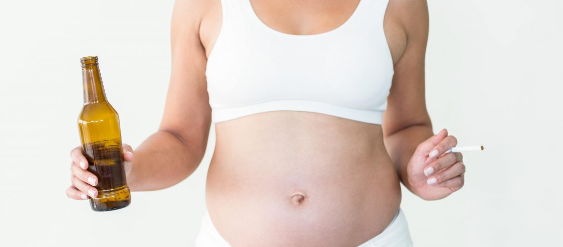 Midsection of pregnant woman holding cigarette and beer bottle against white background