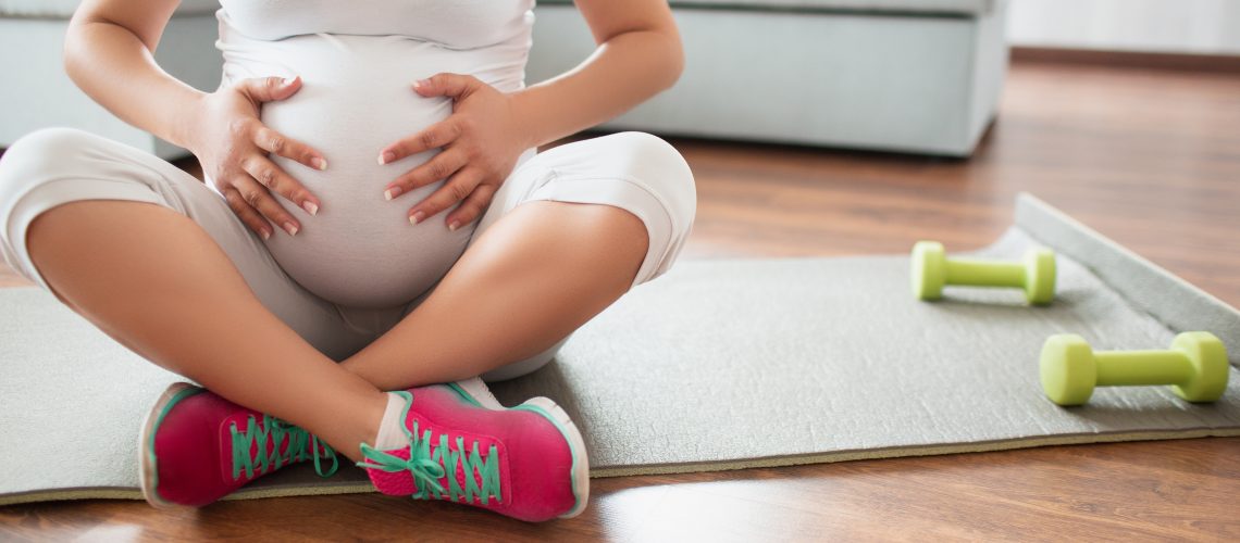 Pregnant woman sitting on an exercise mat with weights next to her